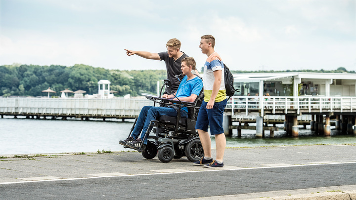 Ottobock Juvo RWD power wheelchair. Wheelchair user and his friends out for a stroll by the harbour.