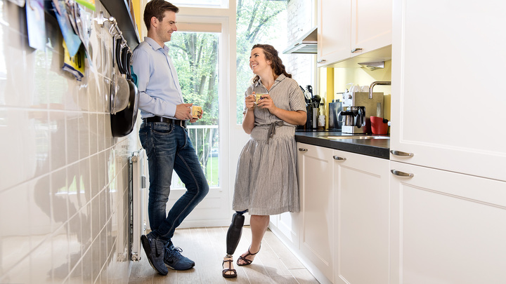 Marije leans to the side against her fridge with her Triton side flex prosthetic foot as she talks to her boyfriend.