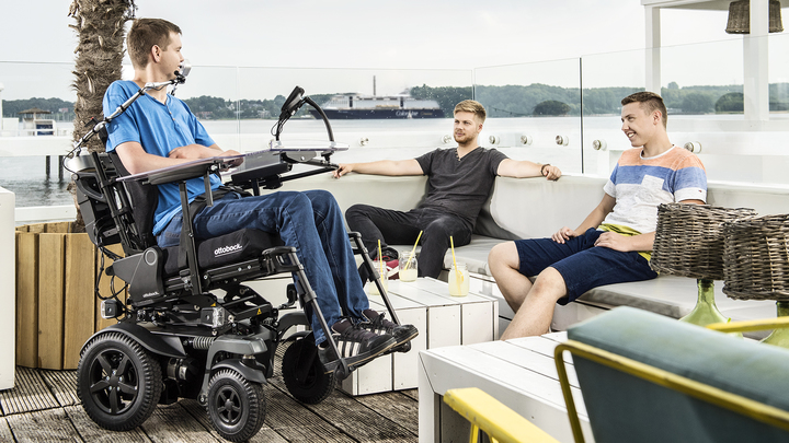 Gebruiker Pierre in zijn Juvo elektrische rolstoel van Ottobock aan het chillen in een café in de haven.