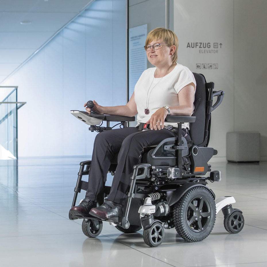 Ottobock Elektrorollstuhl Juvo Anwenderin mit Mittelradantrieb. Stehend in einem Foyer.