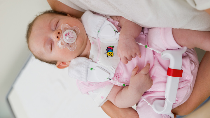 Tilda wears the Tubingen hip flexion and abduction orthosis as she sleeps in her mum’s arms.