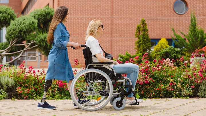 Daniella pushes a wheelchair user along the street.