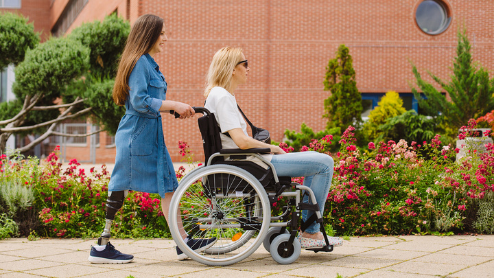 Daniella, tekerlekli sandalyedeki bir kadını cadde boyunca itiyor.