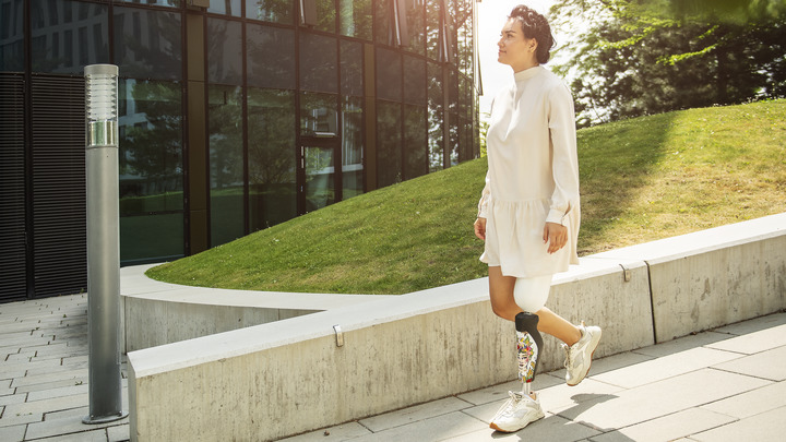 A user with the C-Leg leg prosthesis walking to work outside a glass-fronted office building.