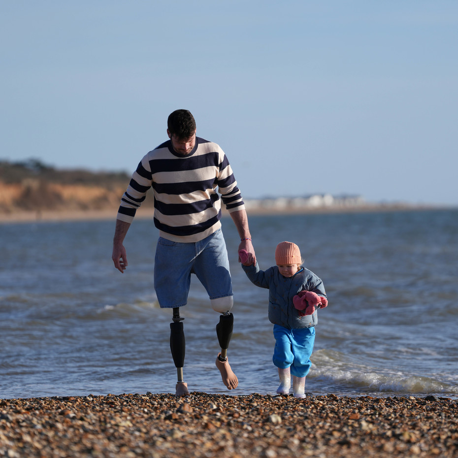 Bilateral Genium X4 user Dave walks on a rocky beach with his daughter
