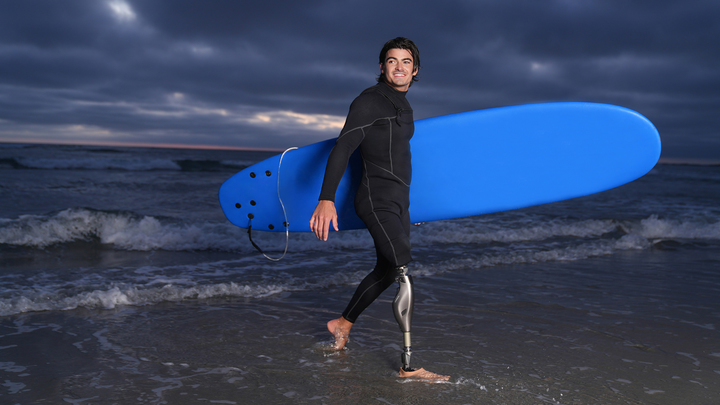 Genium X4 user Caleb carries his surfboard out of the water